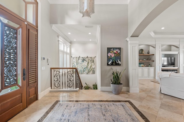 foyer entrance featuring ornamental molding, ornate columns, and a chandelier