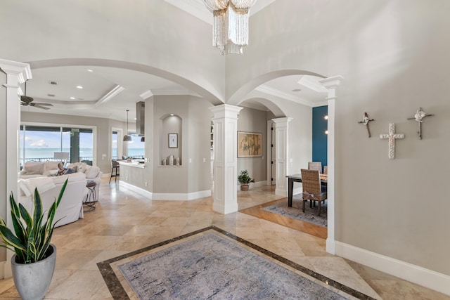 entrance foyer featuring a tray ceiling, ceiling fan with notable chandelier, crown molding, and decorative columns