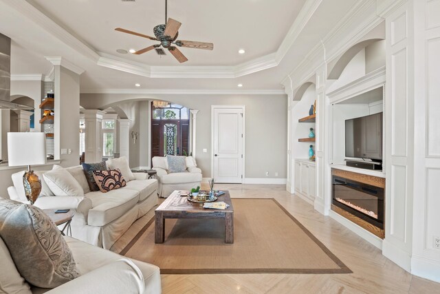 living room featuring light parquet flooring, crown molding, a tray ceiling, and ornate columns