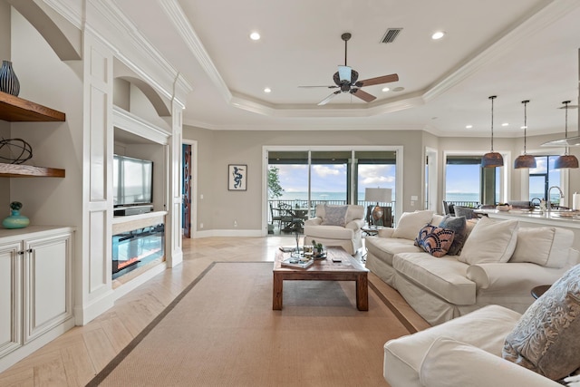 living room featuring a raised ceiling, ceiling fan, sink, and crown molding