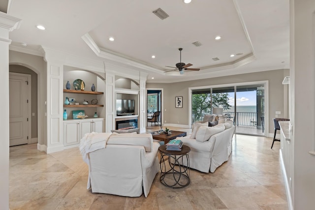 living room with ceiling fan, built in shelves, crown molding, and a raised ceiling