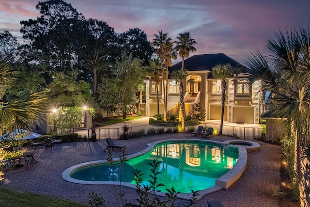 pool at dusk with a patio and an in ground hot tub