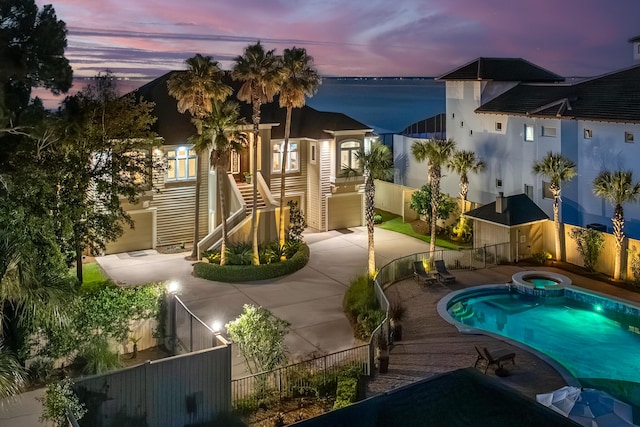 pool at dusk with a water view, a patio area, and an in ground hot tub