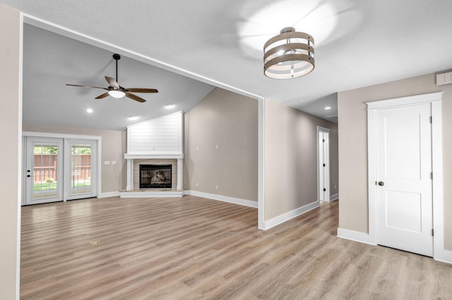 unfurnished living room with a tile fireplace, light wood-type flooring, vaulted ceiling, and ceiling fan