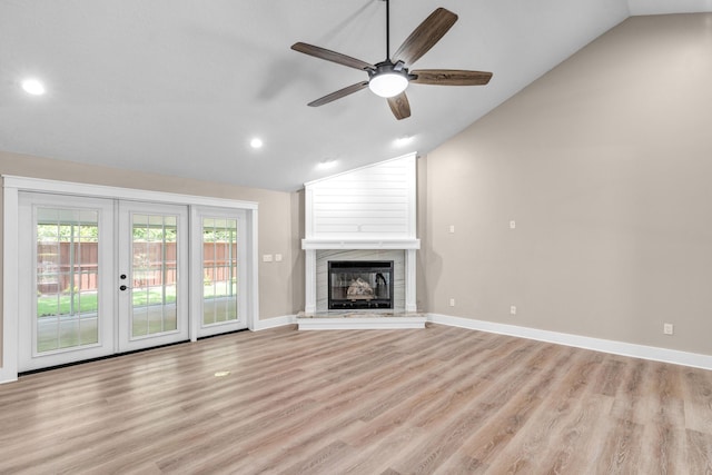 unfurnished living room featuring french doors, vaulted ceiling, ceiling fan, light wood-type flooring, and a tiled fireplace