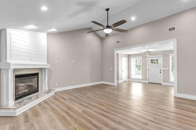 unfurnished living room with ceiling fan, a premium fireplace, a textured ceiling, vaulted ceiling, and light wood-type flooring