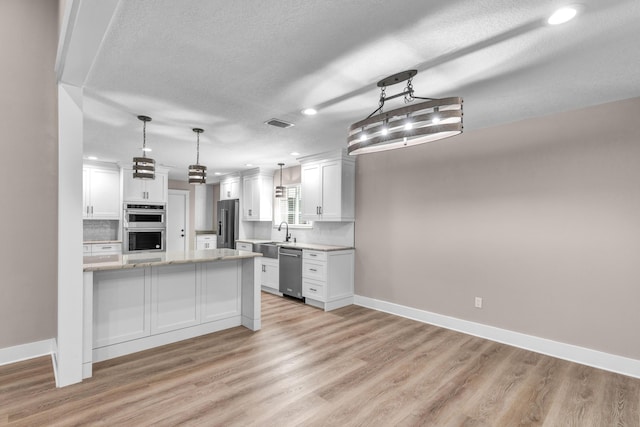 kitchen featuring white cabinets, pendant lighting, backsplash, and stainless steel appliances