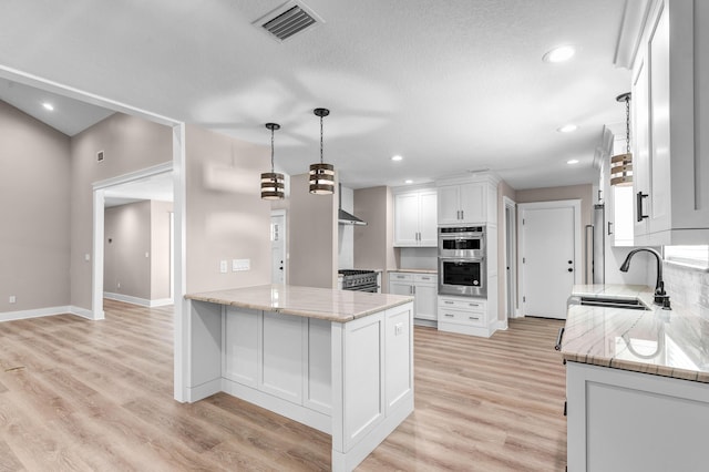 kitchen with kitchen peninsula, light stone counters, white cabinetry, and sink