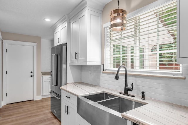 kitchen featuring high end refrigerator, decorative light fixtures, white cabinetry, and sink