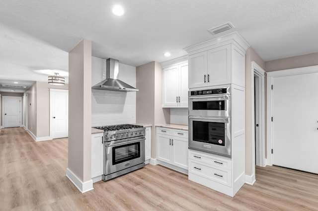 kitchen featuring white cabinets, wall chimney exhaust hood, decorative backsplash, and appliances with stainless steel finishes