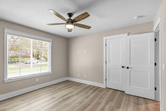 unfurnished bedroom with ceiling fan, a closet, light hardwood / wood-style floors, and a textured ceiling