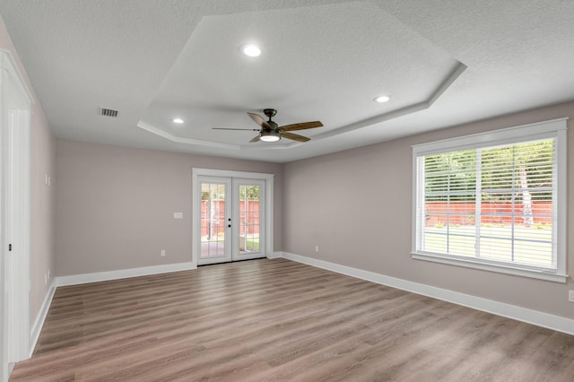 empty room featuring light hardwood / wood-style flooring, a raised ceiling, a textured ceiling, and french doors