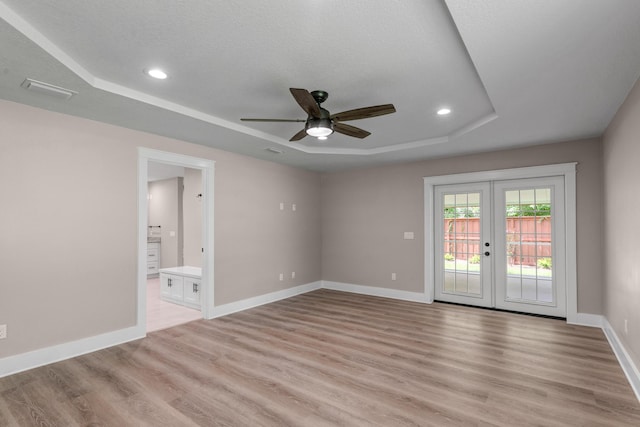 spare room featuring ceiling fan, light hardwood / wood-style floors, french doors, and a tray ceiling