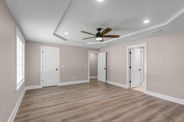 unfurnished bedroom featuring light wood-type flooring, a raised ceiling, and ceiling fan