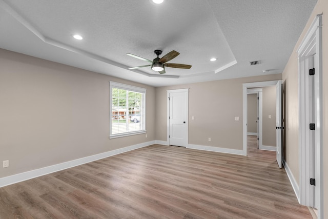 unfurnished bedroom with a textured ceiling, a tray ceiling, ceiling fan, and light hardwood / wood-style floors