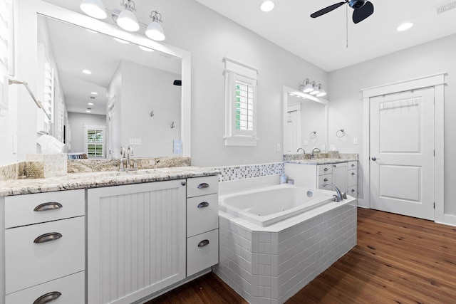 bathroom with ceiling fan, hardwood / wood-style floors, tiled tub, and vanity