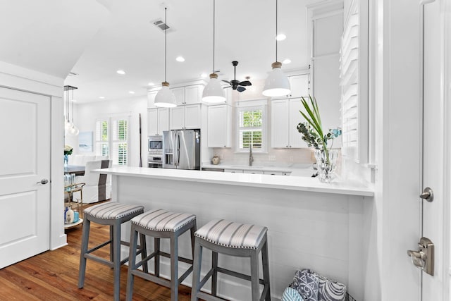 kitchen with appliances with stainless steel finishes, decorative light fixtures, white cabinetry, kitchen peninsula, and a breakfast bar area