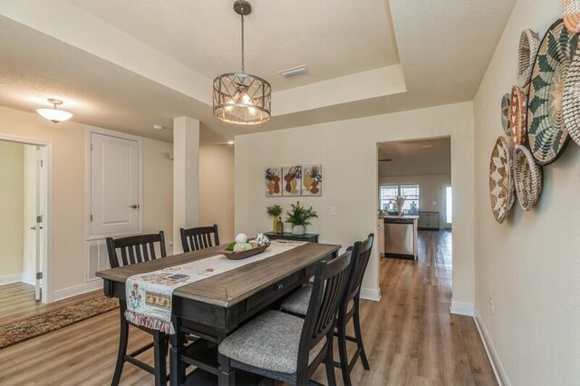 dining area with a notable chandelier, a raised ceiling, and wood-type flooring