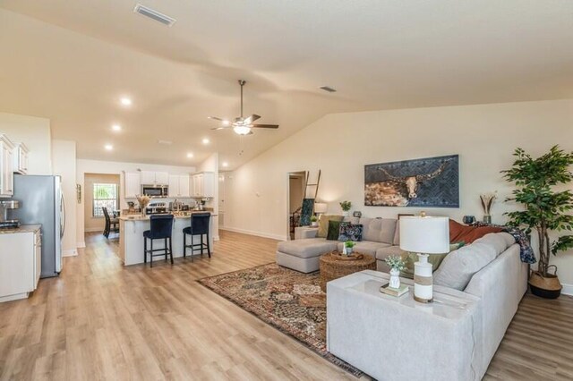 living room with high vaulted ceiling, ceiling fan, and light hardwood / wood-style flooring