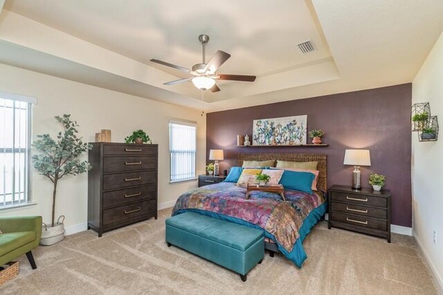 bedroom with light carpet, ceiling fan, and a raised ceiling