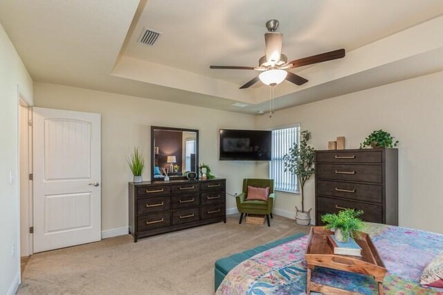 carpeted bedroom with a raised ceiling and ceiling fan