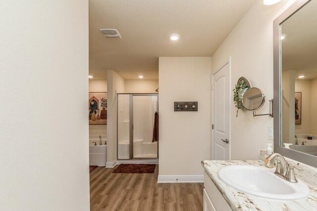 bathroom with hardwood / wood-style flooring, plus walk in shower, and vanity