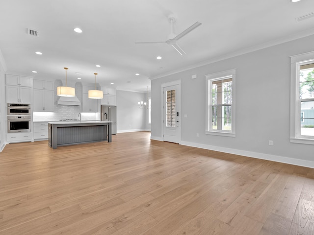 unfurnished living room featuring ceiling fan with notable chandelier, ornamental molding, and light hardwood / wood-style flooring