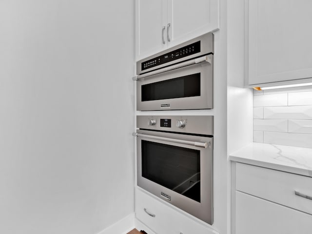 kitchen with decorative backsplash, double oven, light stone counters, and white cabinets