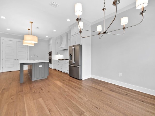 kitchen featuring a kitchen island with sink, light hardwood / wood-style flooring, appliances with stainless steel finishes, decorative light fixtures, and premium range hood