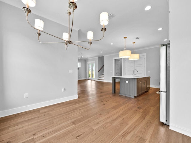 kitchen featuring stainless steel fridge, light hardwood / wood-style floors, ornamental molding, a kitchen island with sink, and sink