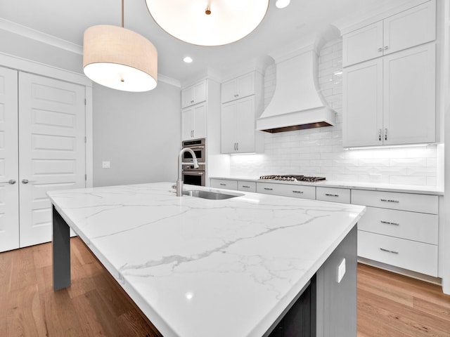 kitchen featuring custom exhaust hood, white cabinets, light hardwood / wood-style flooring, and decorative light fixtures