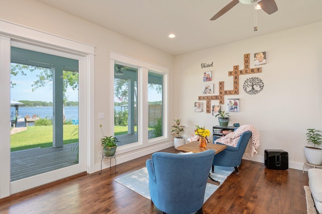 sitting room with dark wood-style floors, a water view, baseboards, and a healthy amount of sunlight