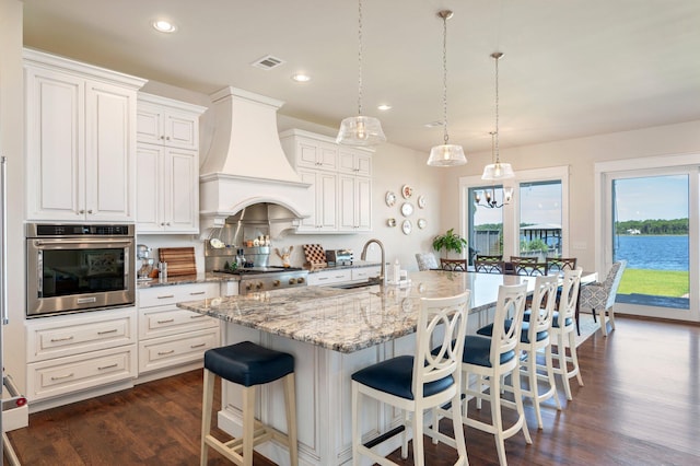 kitchen featuring stainless steel appliances, a sink, hanging light fixtures, custom exhaust hood, and a center island with sink