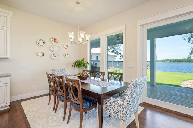 dining area with dark wood-style flooring, a water view, an inviting chandelier, and baseboards