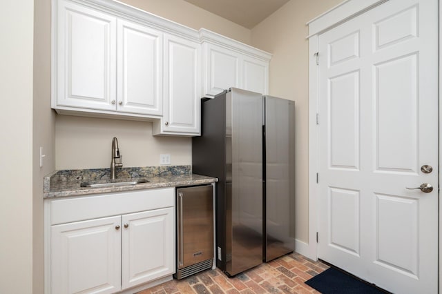 kitchen featuring white cabinetry, light stone counters, a sink, and freestanding refrigerator