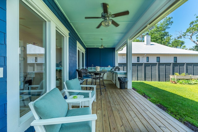 wooden deck featuring ceiling fan, fence, outdoor dining area, and a lawn