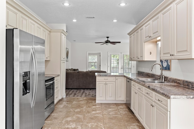 kitchen featuring ceiling fan, sink, stainless steel appliances, kitchen peninsula, and cream cabinetry