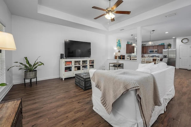 living room with a tray ceiling, ceiling fan, and dark wood-type flooring