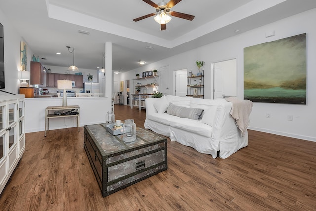 living room with dark hardwood / wood-style floors, ceiling fan, and a raised ceiling