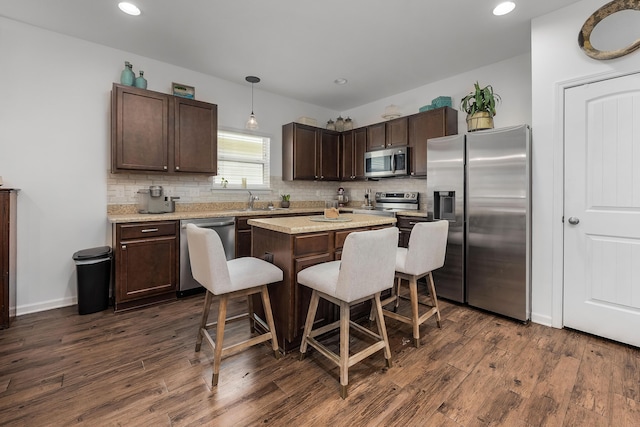 kitchen with pendant lighting, a breakfast bar, dark hardwood / wood-style floors, appliances with stainless steel finishes, and a kitchen island