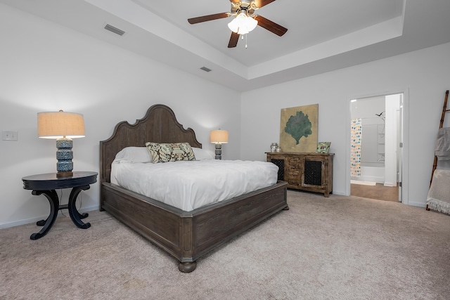 carpeted bedroom featuring ceiling fan, a raised ceiling, and ensuite bath