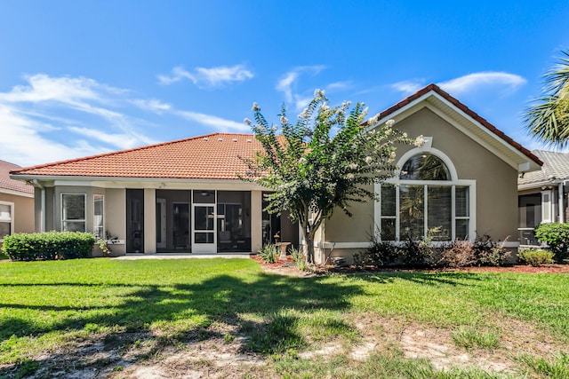 rear view of property with a sunroom, a lawn, a tiled roof, and stucco siding