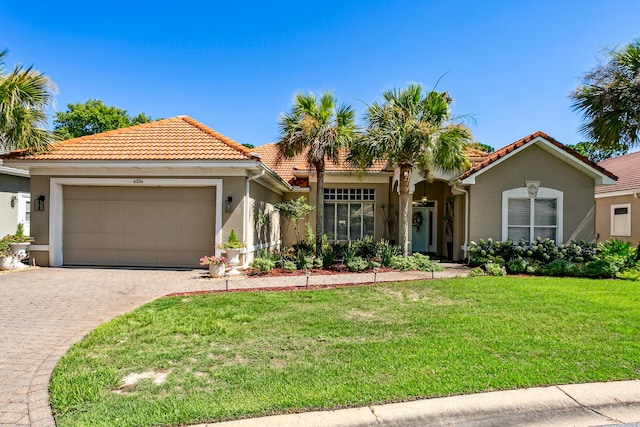 mediterranean / spanish home with a front yard, a tiled roof, an attached garage, and stucco siding