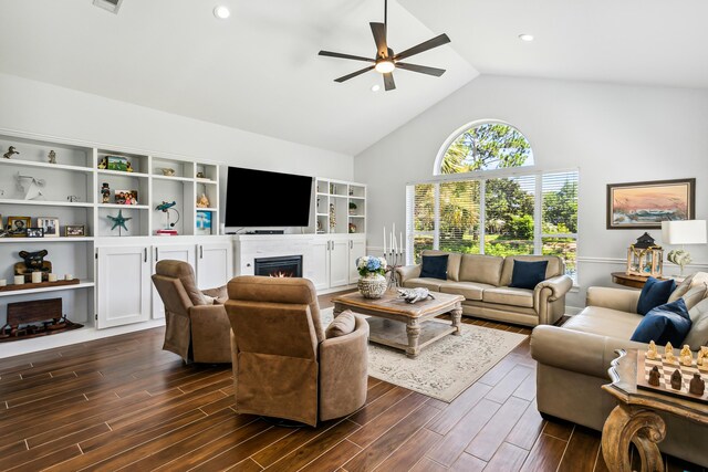 living room with ceiling fan, a lit fireplace, dark wood-type flooring, and high vaulted ceiling