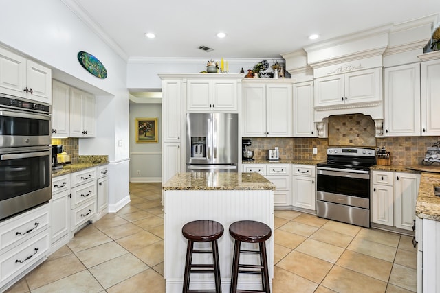 kitchen with light tile patterned floors, a kitchen island, appliances with stainless steel finishes, and crown molding