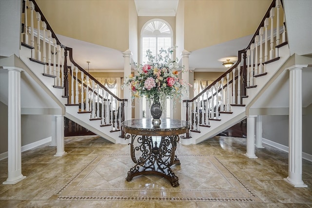 foyer entrance featuring ornate columns, a towering ceiling, light tile flooring, and crown molding