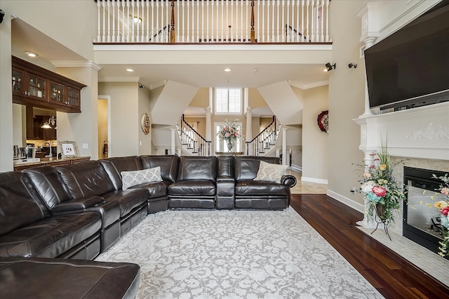 living room featuring a premium fireplace, crown molding, dark hardwood / wood-style floors, and a towering ceiling