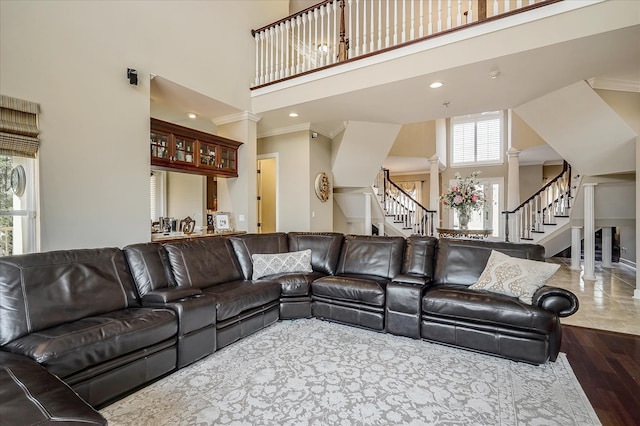 living room featuring a towering ceiling, crown molding, wood-type flooring, and ornate columns