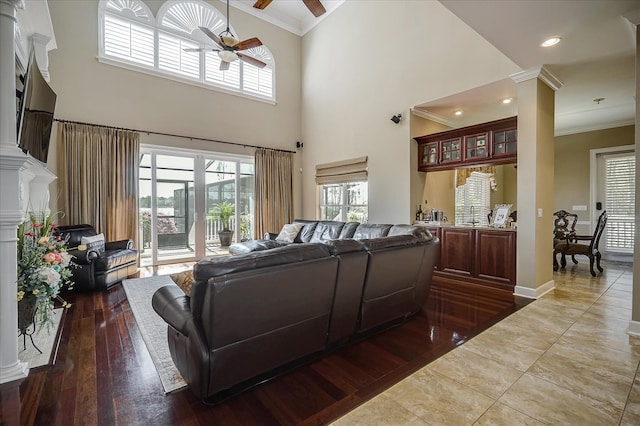 living room featuring ceiling fan, decorative columns, a high ceiling, ornamental molding, and hardwood / wood-style flooring