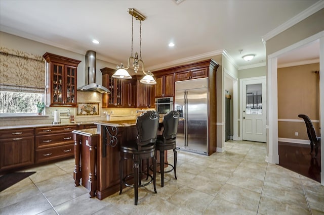 kitchen with a center island, hanging light fixtures, stainless steel appliances, wall chimney exhaust hood, and tasteful backsplash